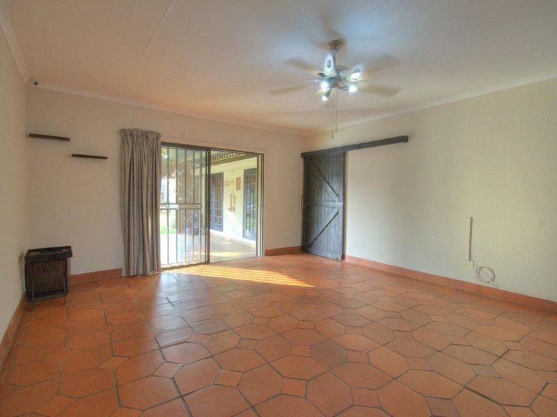 Spacious living area featuring terracotta tile flooring, a ceiling fan, and a sliding door providing access to the outdoor patio.