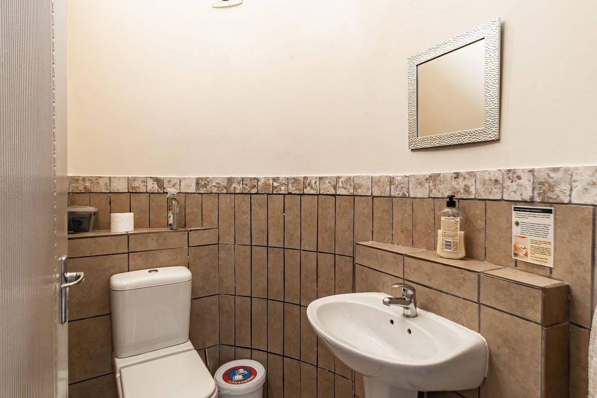 A compact office restroom featuring a pedestal sink, a standard toilet, and tiled wall finishes with a decorative border.
