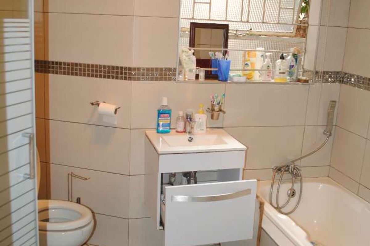 A compact bathroom featuring a bathtub, a wall-mounted vanity unit, a toilet, and a glass-enclosed shower, finished with neutral wall and floor tiles.
