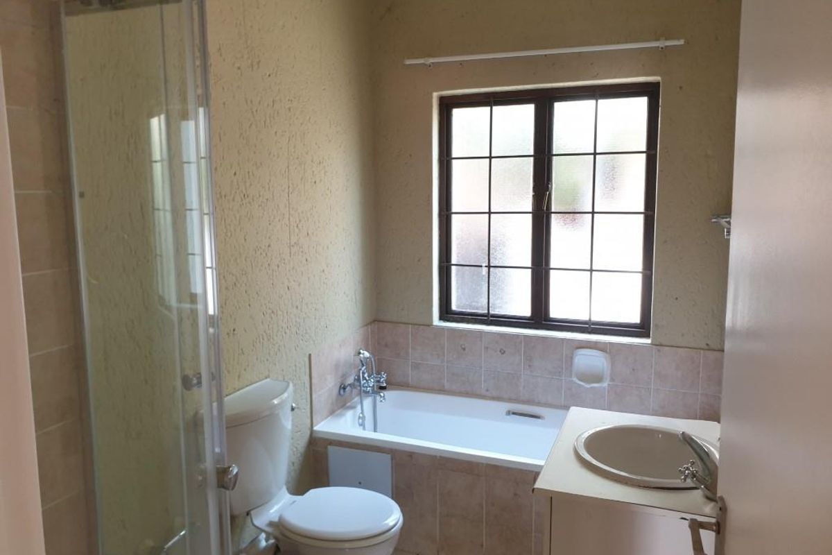 A functional bathroom featuring a built-in bathtub, separate shower enclosure, toilet, and vanity basin with tiled splashbacks and a window for natural light.