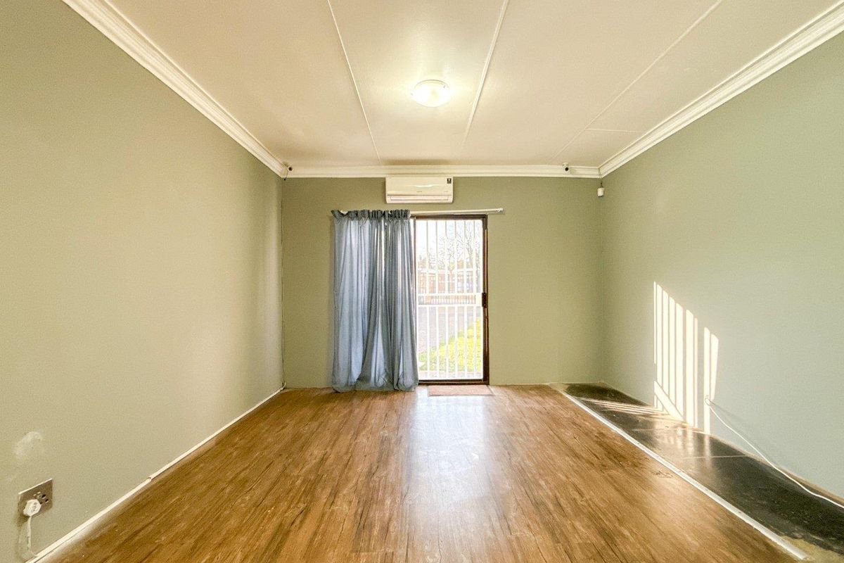 A spacious, empty living room featuring laminate flooring, coving, and a split-system air conditioner, with direct access to the exterior via a sliding glass door.