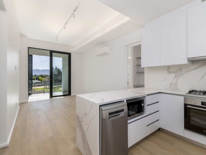 Modern open-plan kitchen and living area featuring high-end finishes, stone countertops, integrated appliances, and seamless access to a private balcony with scenic views.