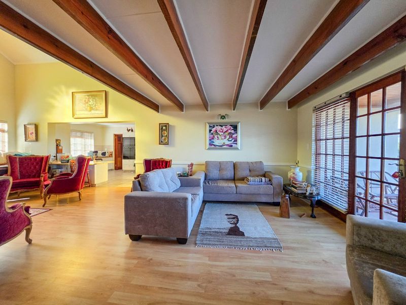 Spacious open-plan living area featuring exposed timber ceiling beams, laminate flooring, and seamless flow to the kitchen and outdoor patio through sliding glass doors.