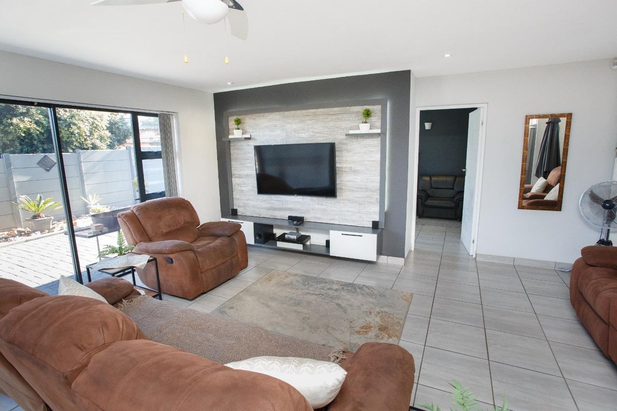 A well-maintained living room featuring tiled flooring, a modern built-in media wall unit, and large sliding glass doors providing access to the patio.