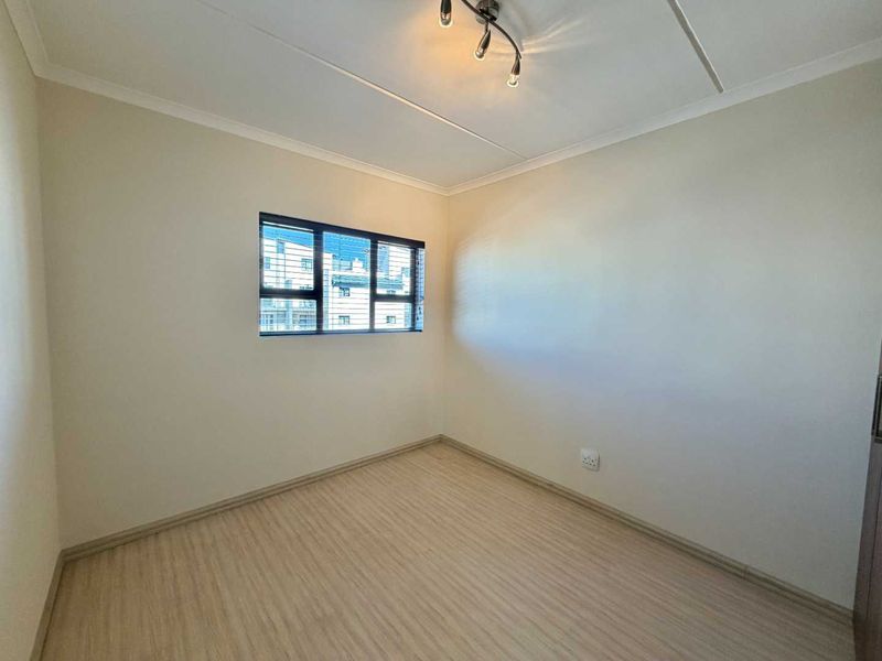 A clean, empty bedroom featuring light-toned laminate flooring, neutral walls, and a modern aluminium-framed window.