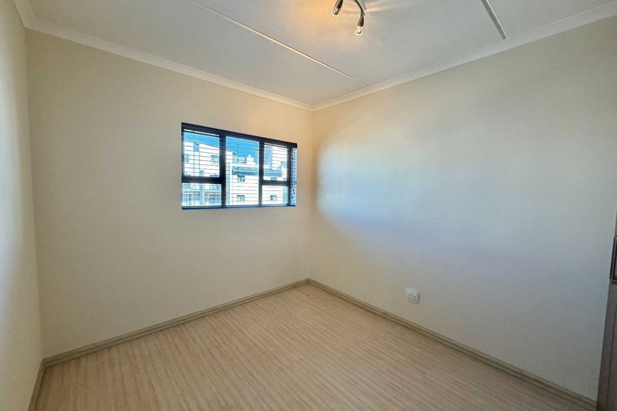 A clean, empty bedroom featuring light-toned laminate flooring, neutral walls, and a modern aluminium-framed window.