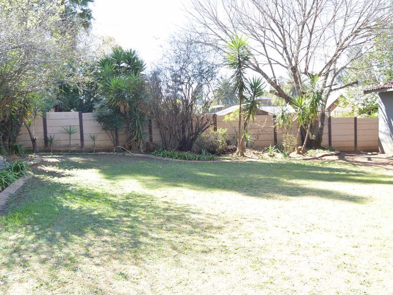 A spacious private garden featuring a well-maintained lawn, mature trees, and a secure precast concrete boundary wall.
