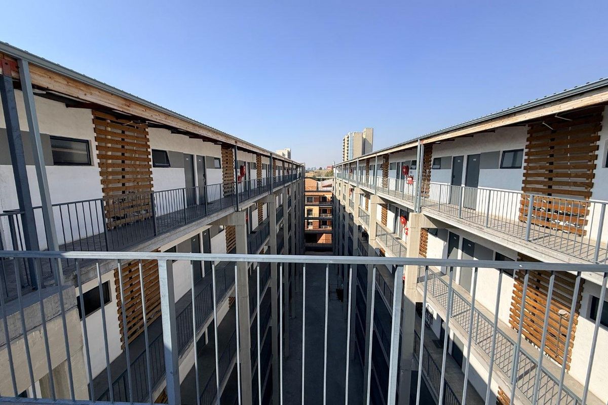 View of the apartment complex exterior walkways and central courtyard area featuring modern metal railings and timber architectural detailing.