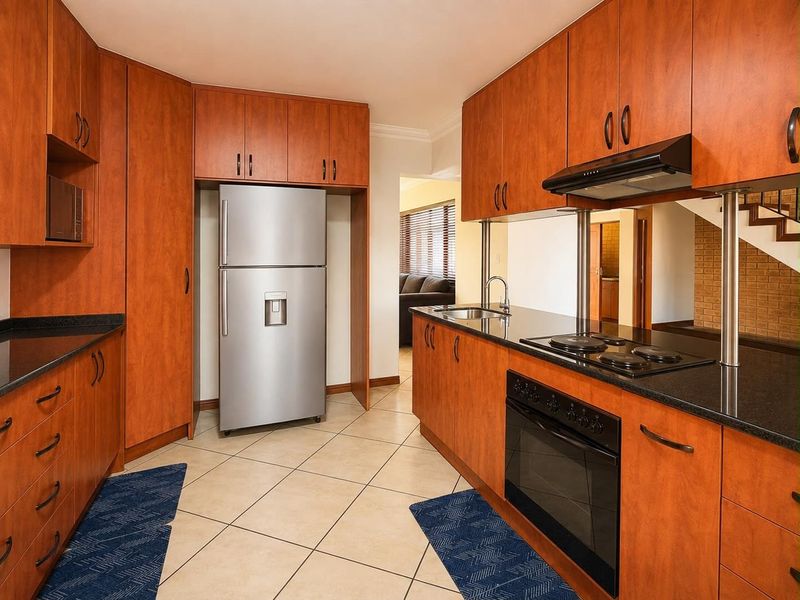 Functional kitchen featuring warm-toned laminate cabinetry, granite countertops, built-in oven, electric hob, and tiled flooring.