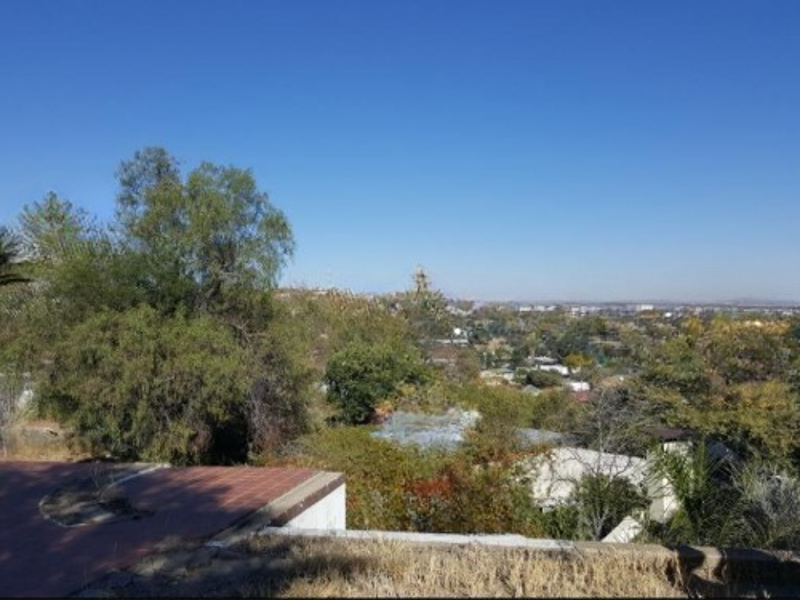 An elevated view overlooking a lush, tree-filled landscape and residential neighborhood under a clear blue sky.