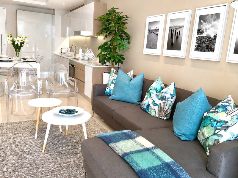 Modern open-plan living area featuring a sleek kitchen with integrated appliances, stone countertops, and neutral cabinetry, seamlessly flowing into the lounge space.