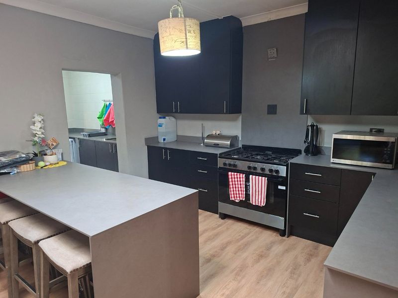 Modern kitchen featuring dark cabinetry, stone countertops, a central island, and a gas stove, with an adjacent scullery area.