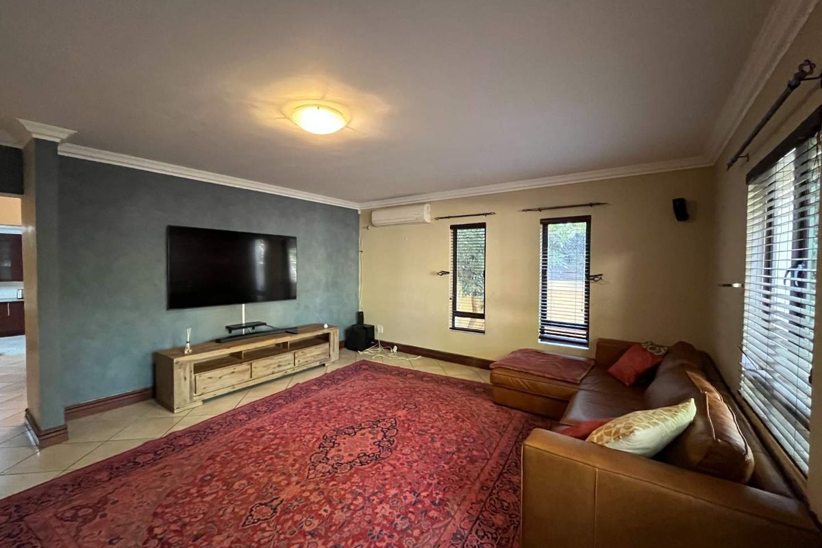 Spacious living room featuring tiled flooring, a feature accent wall, split-system air conditioning, and large windows with fitted blinds.