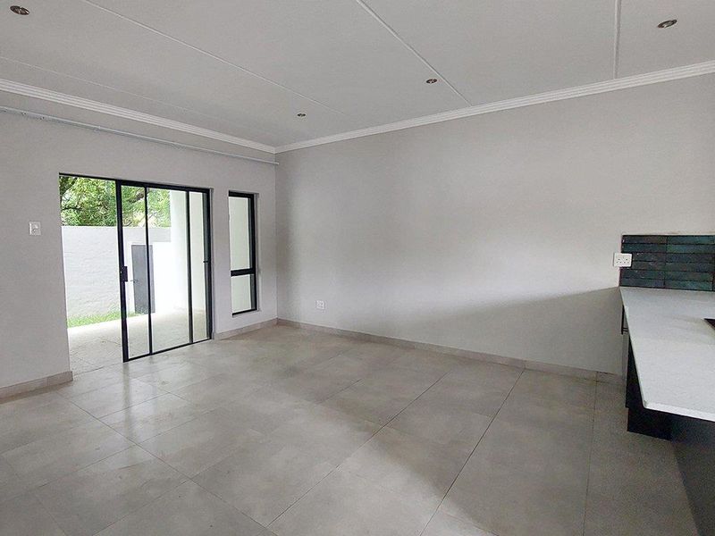 Spacious open-plan living area featuring modern tiled floors, recessed lighting, and a sleek kitchen corner with a built-in hob and stone countertop.