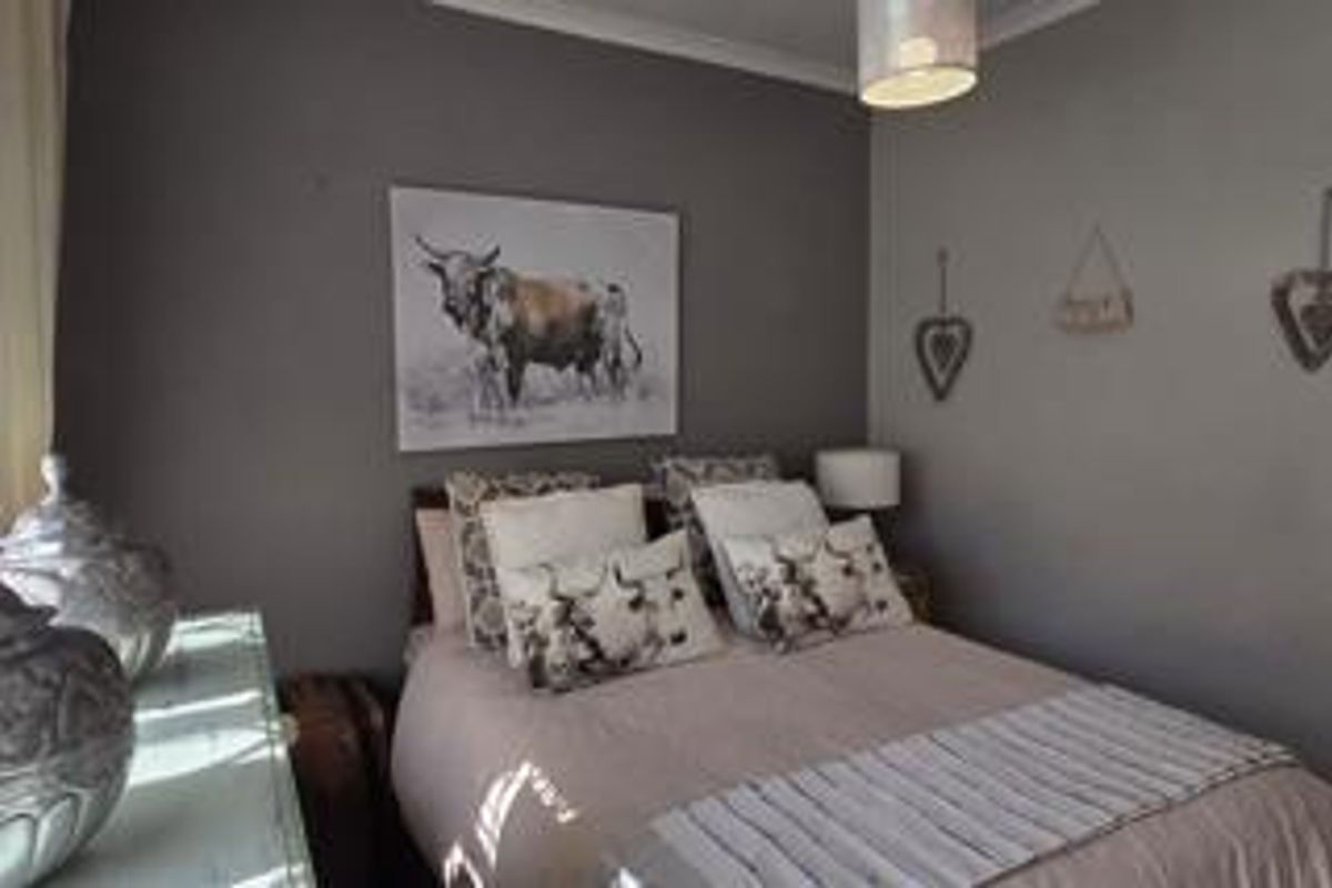 A cozy bedroom featuring neutral wall tones, crown molding, and a central light fixture, providing a comfortable and functional sleeping space.