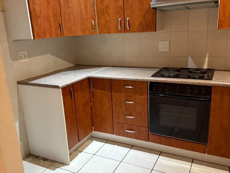 A functional kitchen featuring wood-look cabinetry, built-in oven and hob, extractor fan, and tiled flooring. The space is clean and ready for updates.