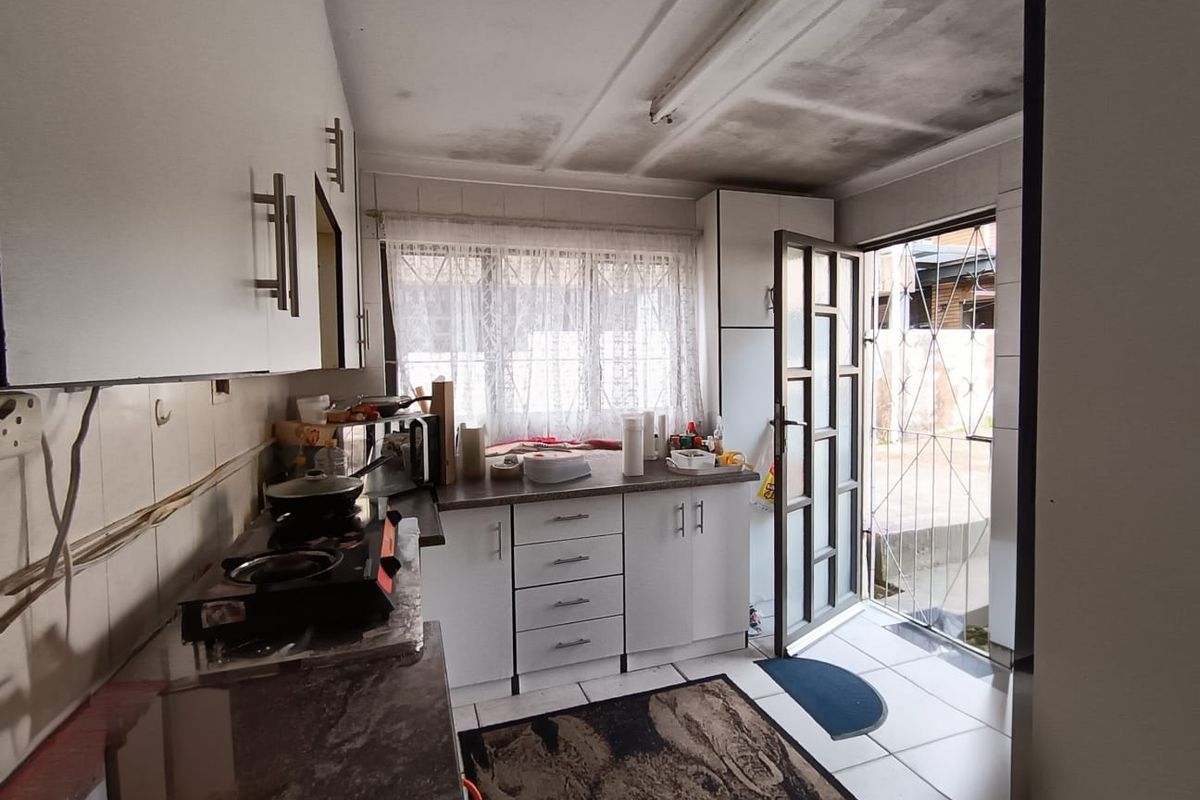 A functional kitchen featuring built-in cabinetry, tiled flooring, and direct exterior access via a security gate, showing signs of ceiling wear.