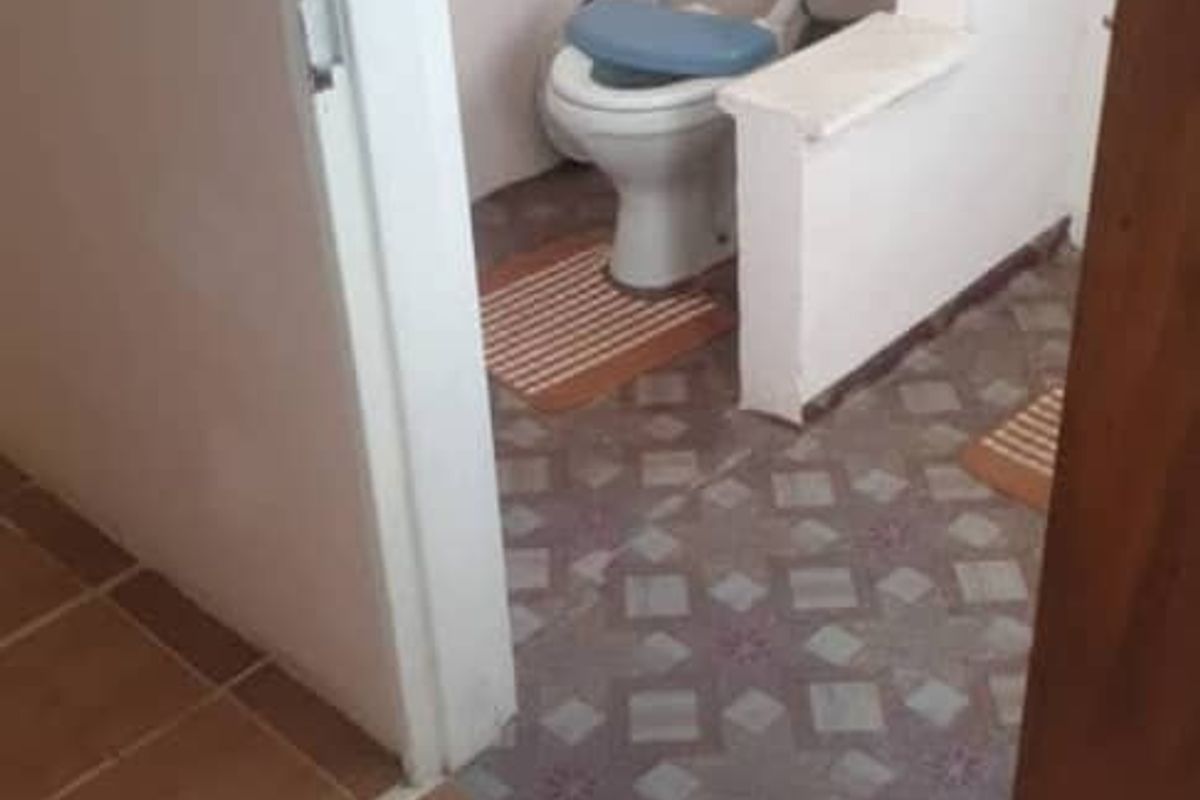 A small, dated bathroom featuring a traditional toilet and patterned floor tiles, requiring modernization and cosmetic updates.
