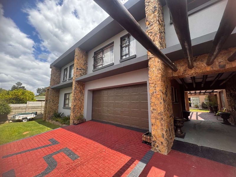 Front elevation featuring a double garage, stone-clad pillars, and a paved driveway with a covered entrance area.