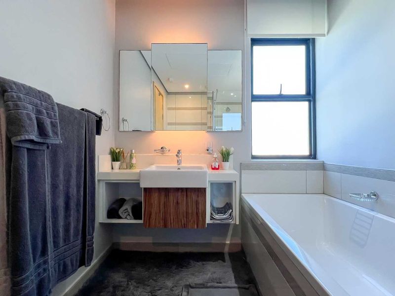 A modern bathroom featuring a floating vanity with integrated basin, a large bathtub, and a triple-panel mirrored cabinet.