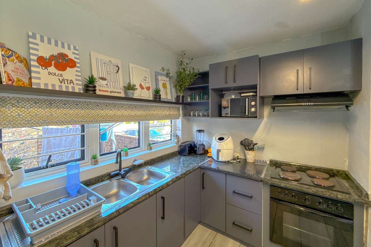 A functional kitchen featuring dark grey cabinetry, granite countertops, a double basin sink, and integrated electric cooking appliances.