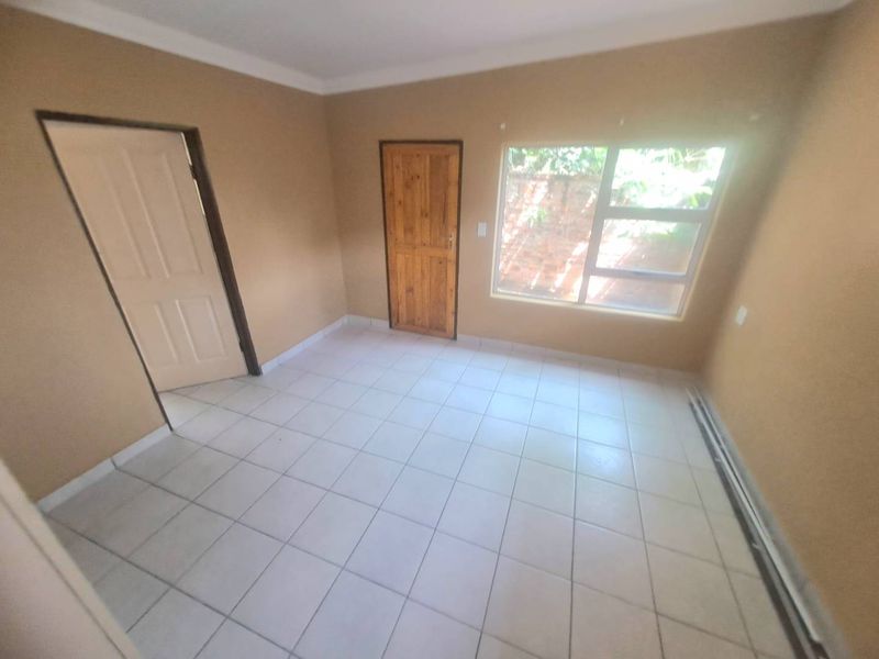 A vacant bedroom featuring neutral wall paint, tiled flooring, and a large window providing natural light.