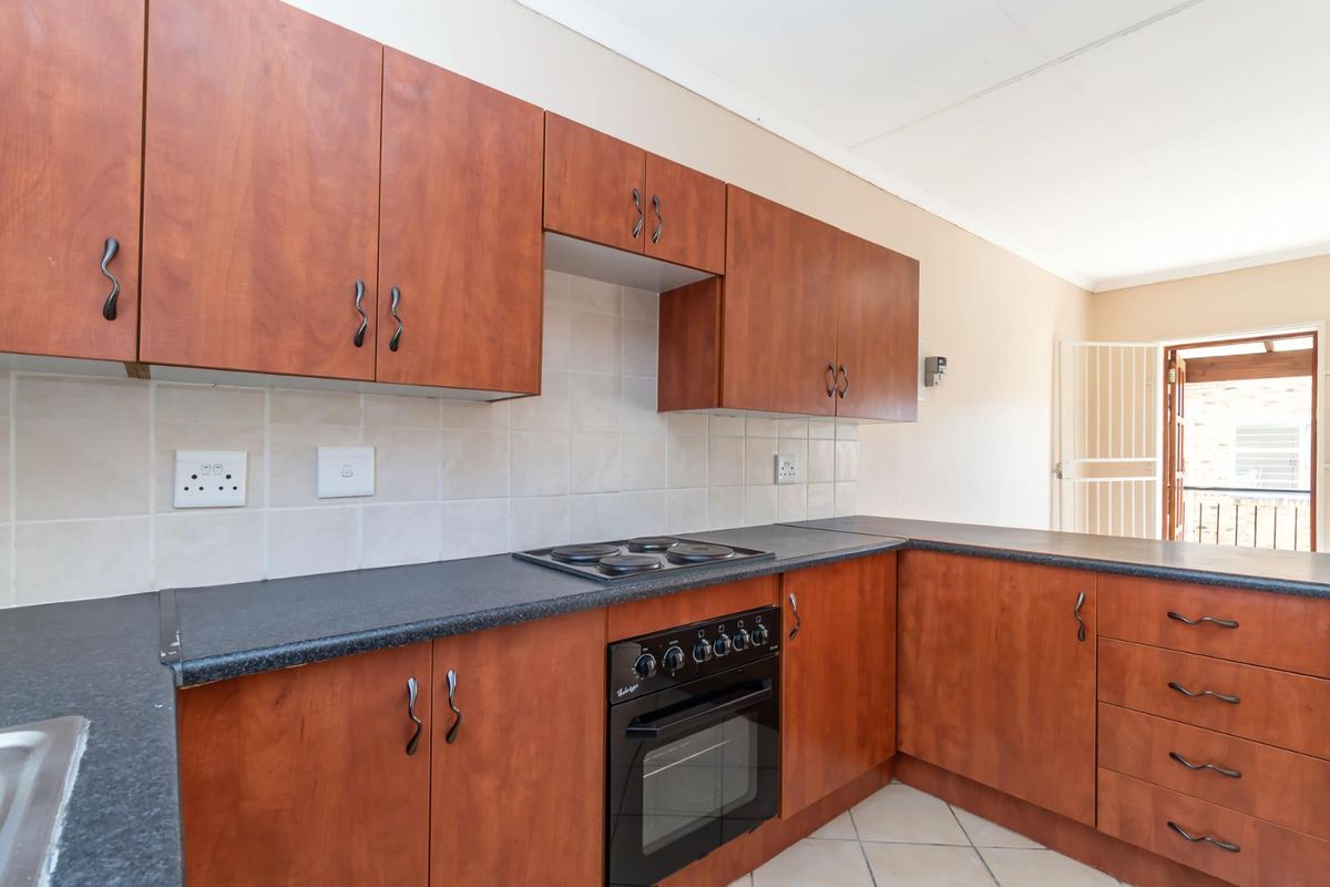 Functional kitchen featuring wood-look cabinetry, dark laminate countertops, built-in oven, and electric hob with tiled backsplash.