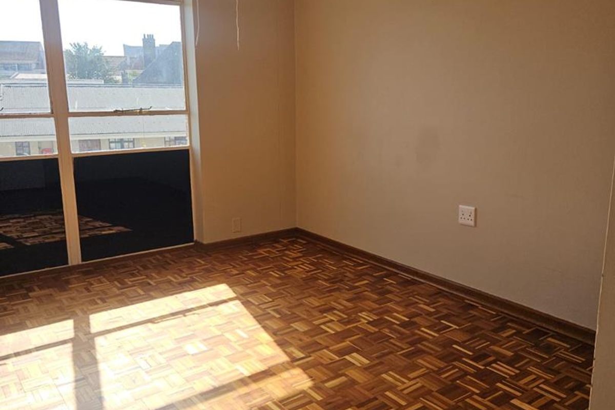 A bright, empty bedroom featuring classic parquet flooring, a ceiling fan, and large windows providing natural light.