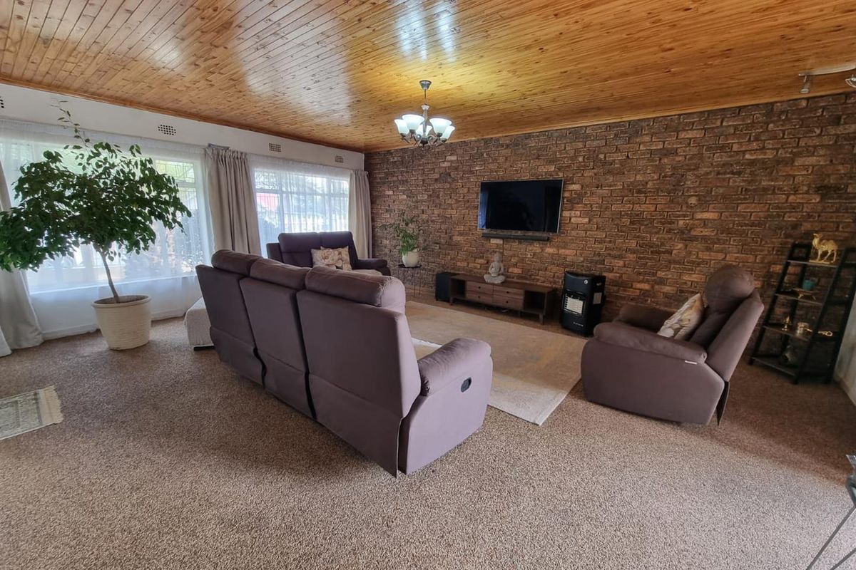 Spacious living room featuring a prominent exposed brick feature wall, timber-clad ceiling, and large windows allowing for ample natural light.