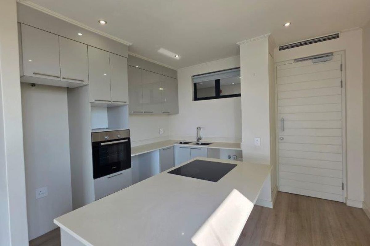 Modern kitchen featuring sleek cabinetry, stone countertops, integrated oven, and a central island with an electric cooktop in a bright, open-plan layout.