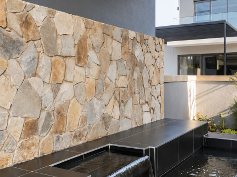 A modern outdoor water feature with a stone-clad wall and dark tiled surround, creating a sophisticated architectural focal point.