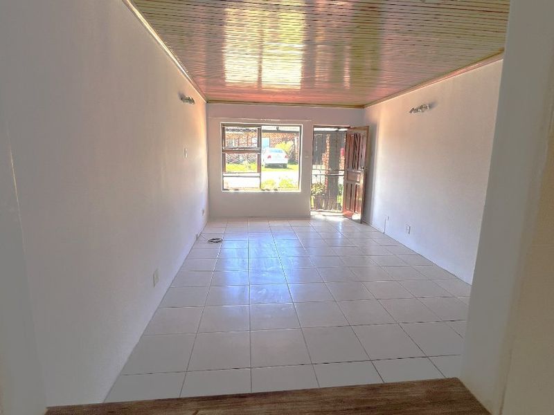 An empty, open-plan living area featuring tiled flooring and a timber-clad ceiling, with direct access to the exterior through a security door.