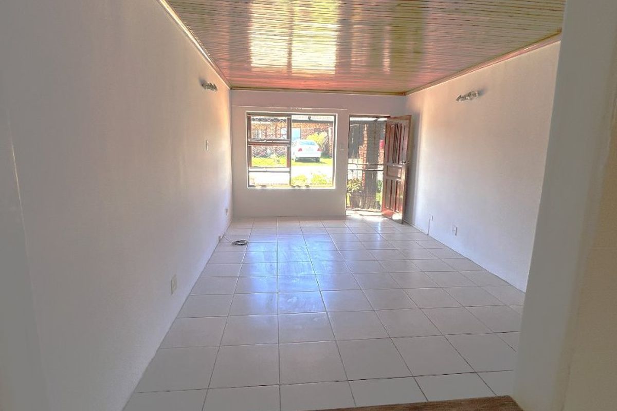 An empty, open-plan living area featuring tiled flooring and a timber-clad ceiling, with direct access to the exterior through a security door.