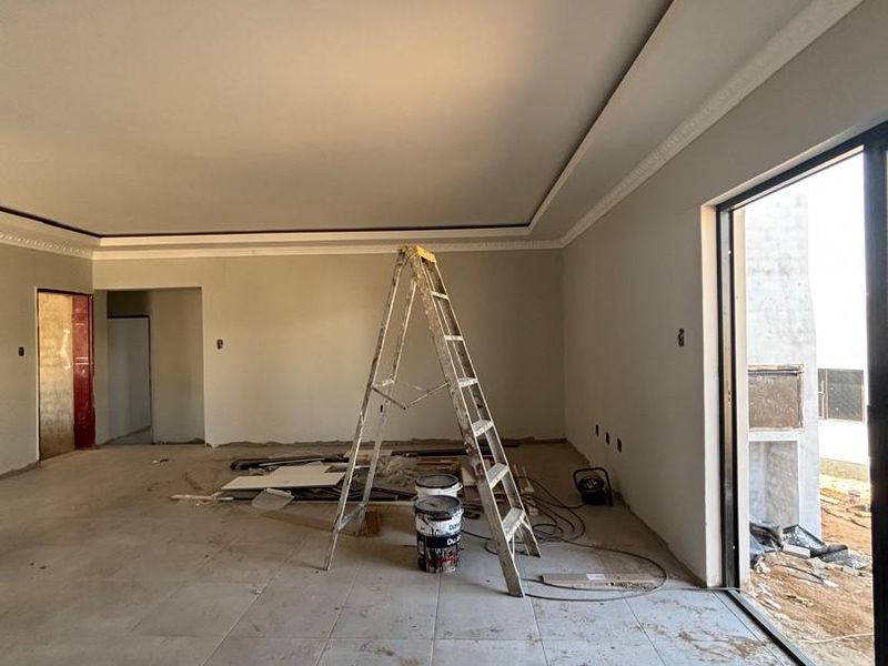 Spacious living area currently under construction, featuring recessed ceilings, cove molding, and large sliding glass doors leading to an outdoor space.