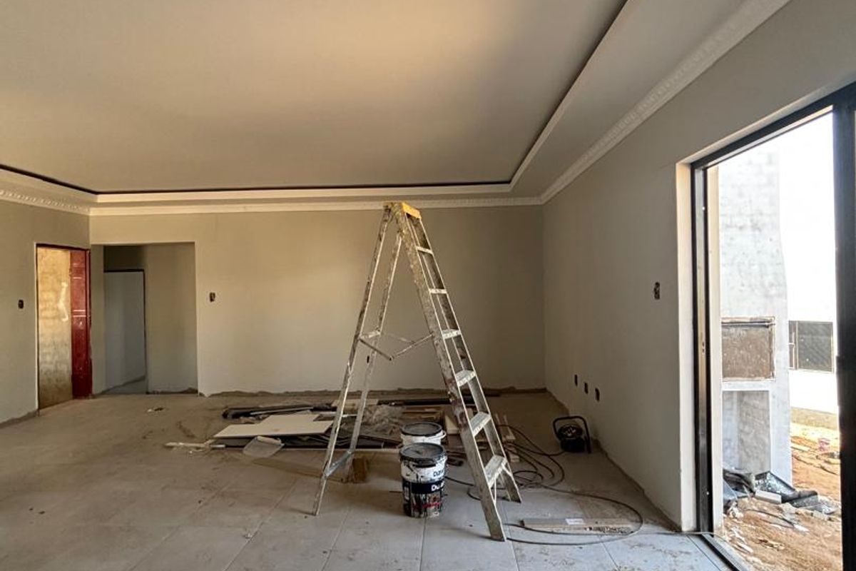 Spacious living area currently under construction, featuring recessed ceilings, cove molding, and large sliding glass doors leading to an outdoor space.