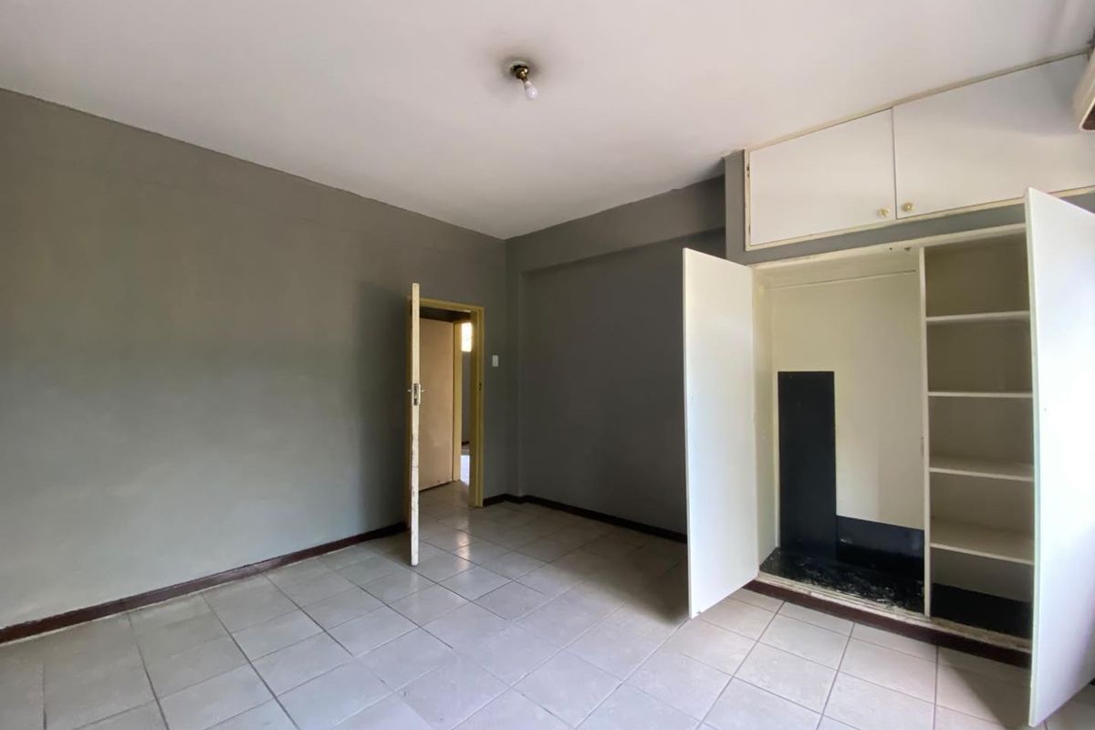 A vacant bedroom featuring tiled flooring, built-in storage cupboards with overhead cabinets, and a neutral grey wall finish.