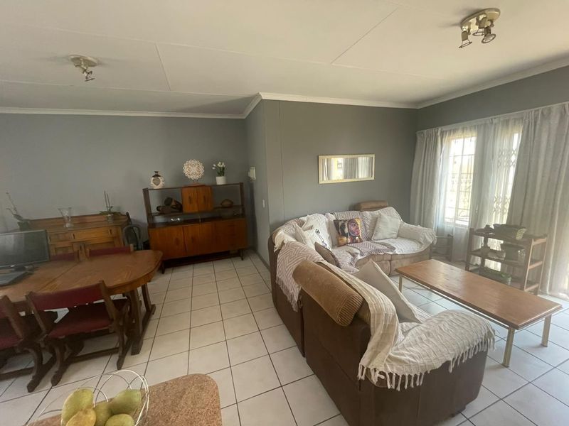 Spacious open-plan living and dining area featuring neutral wall tones, ceramic floor tiles, and natural light through large windows with security gates.