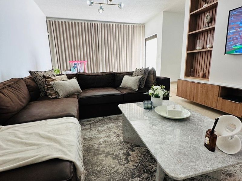 A well-maintained living room featuring a custom built-in wooden shelving unit and media cabinet, complemented by neutral finishes and ample natural light.