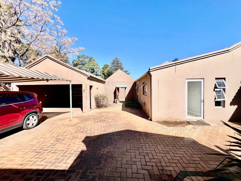 Exterior view of the property featuring a brick-paved driveway, a double garage with an awning, and access to the main building entrance.