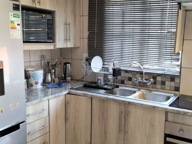 A functional kitchen featuring light wood-look cabinetry, laminate countertops, a double stainless steel sink, and integrated appliances including an oven and microwave.
