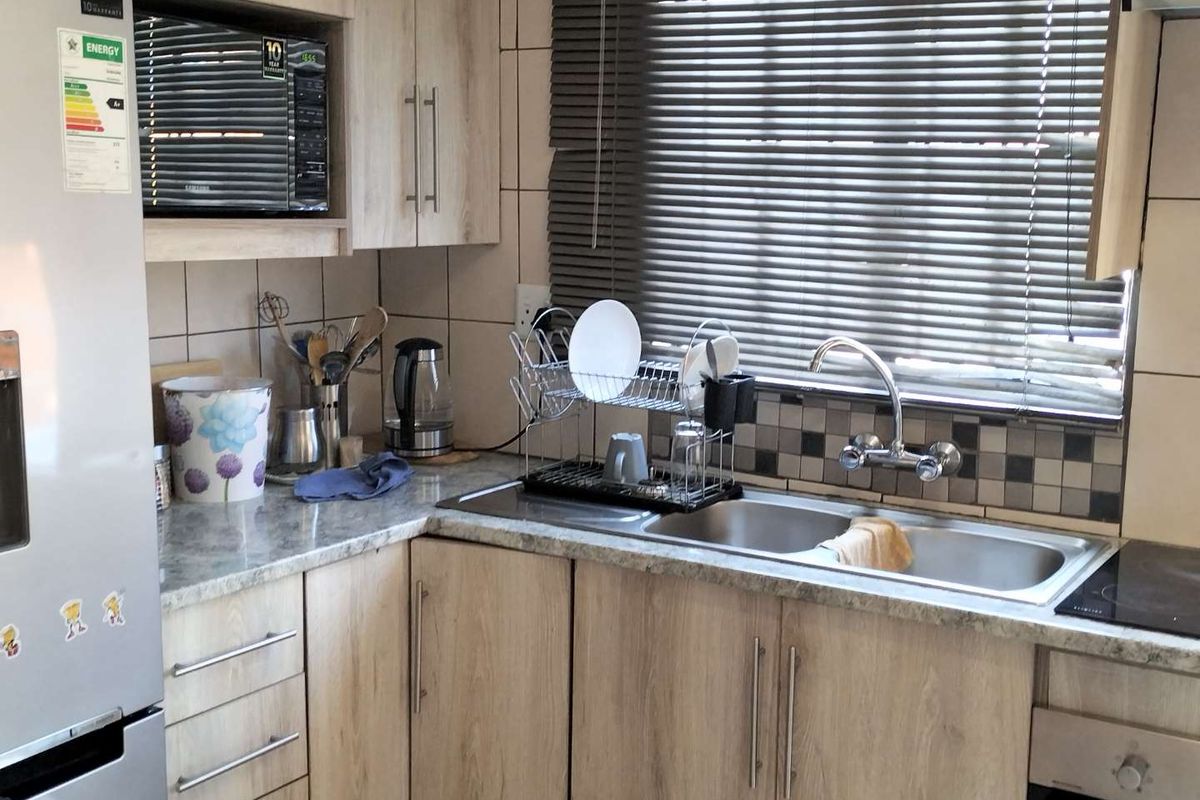 A functional kitchen featuring light wood-look cabinetry, laminate countertops, a double stainless steel sink, and integrated appliances including an oven and microwave.