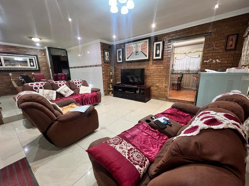 Spacious living room featuring exposed brick walls, tiled flooring, and recessed lighting, with an open transition to the adjacent kitchen area.