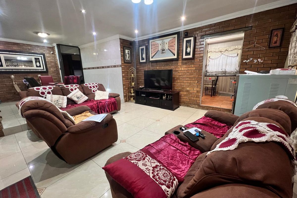 Spacious living room featuring exposed brick walls, tiled flooring, and recessed lighting, with an open transition to the adjacent kitchen area.