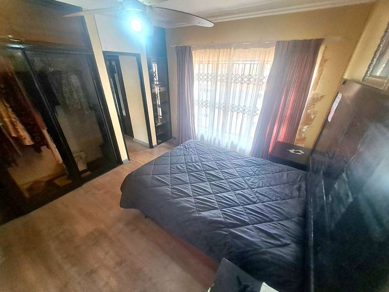 Bedroom featuring built-in cupboards, laminate flooring, and a ceiling fan, with visible wall surface damage requiring repair and cosmetic attention.