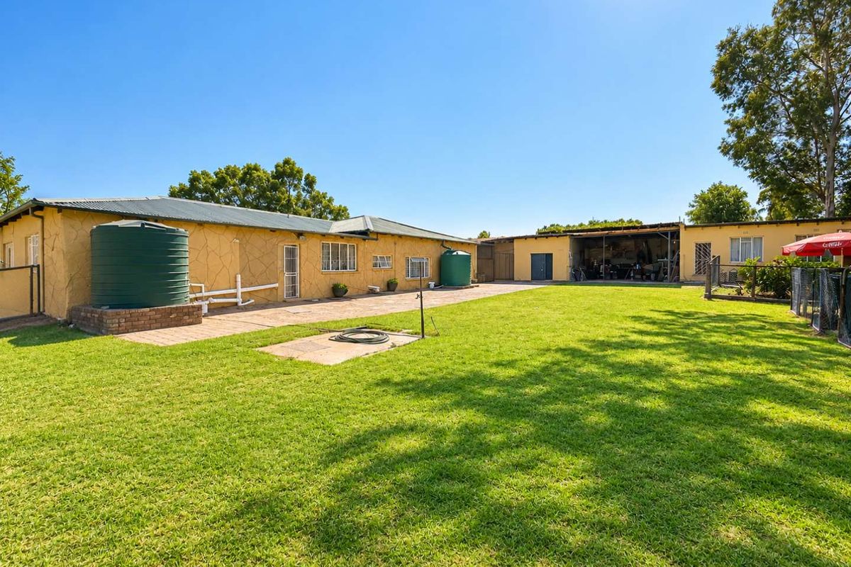 Spacious rear garden area featuring a large lawn, paved pathways, and multiple water storage tanks adjacent to the main dwelling and outbuilding.