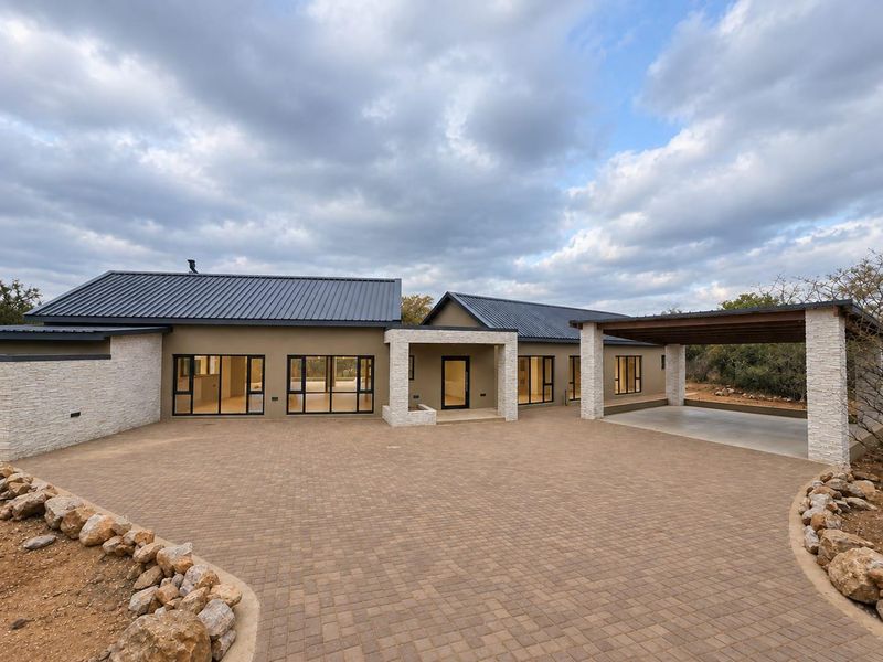 Modern single-story residence featuring a paved driveway, stone-clad accents, metal roofing, and an integrated carport, showcasing contemporary architectural design.