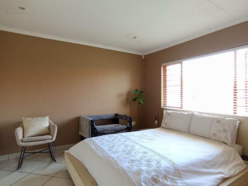 A well-lit bedroom featuring neutral-toned walls, tiled flooring, and built-in cupboards, offering a functional and comfortable living space.