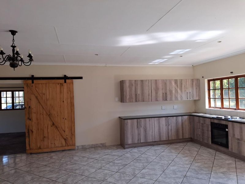 A spacious kitchen featuring modern wood-look cabinetry, built-in oven, hob, tiled flooring, and a rustic sliding barn door, offering a clean and functional layout.