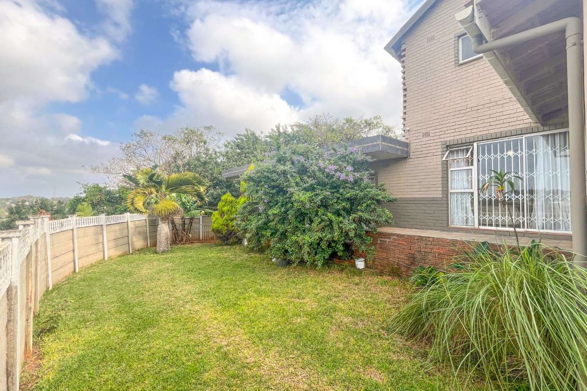 A private rear garden featuring a lawn area, established landscaping, and a brick-built house exterior with security gates on windows.