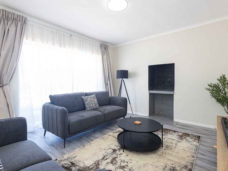 A bright and modern living room featuring laminate flooring, a built-in fireplace, and large windows with curtain tracks.